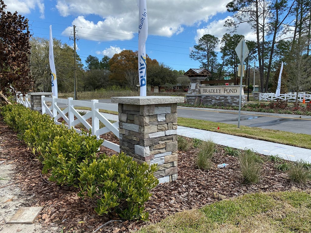 Photo of neighborhood entrance with pretty white horse fence and stone pillar.