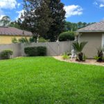Grassy backyard with vinyl fence and pretty landscaping.