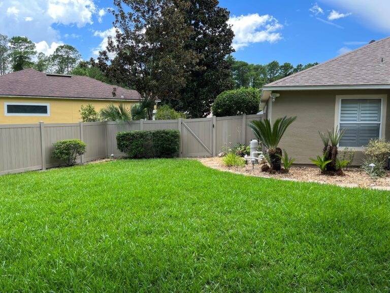 Grassy backyard with vinyl fence and pretty landscaping.