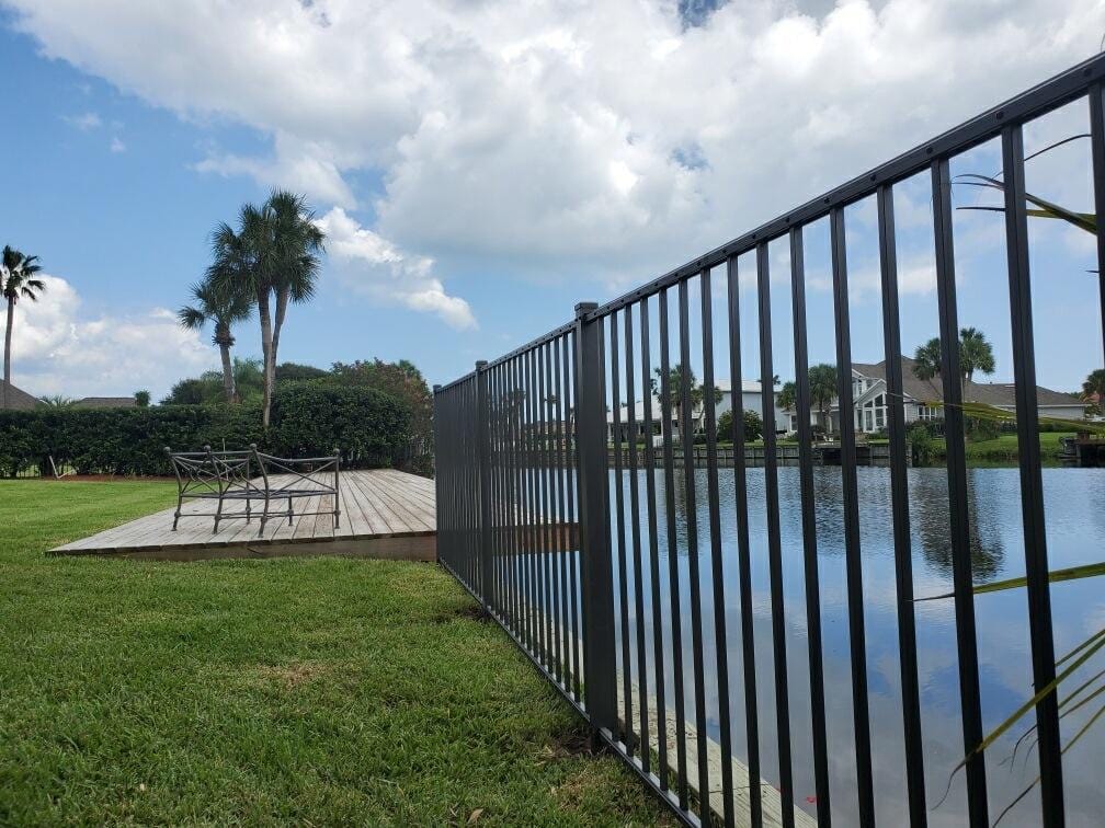 Black aluminum fence on a property line, along a waterway.