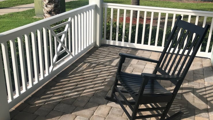 Porch with while railing and rocking chair and a paver floor.