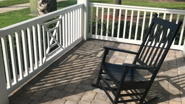 Porch with while railing and rocking chair and a paver floor.