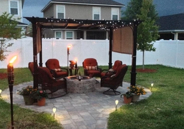 Backyard fire pit and chairs surrounding it with torches lit for evening ambiance.