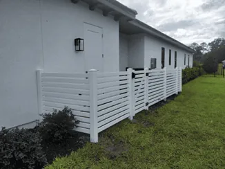 White vinyl fence surrounding backyard equipment and garbage cans.
