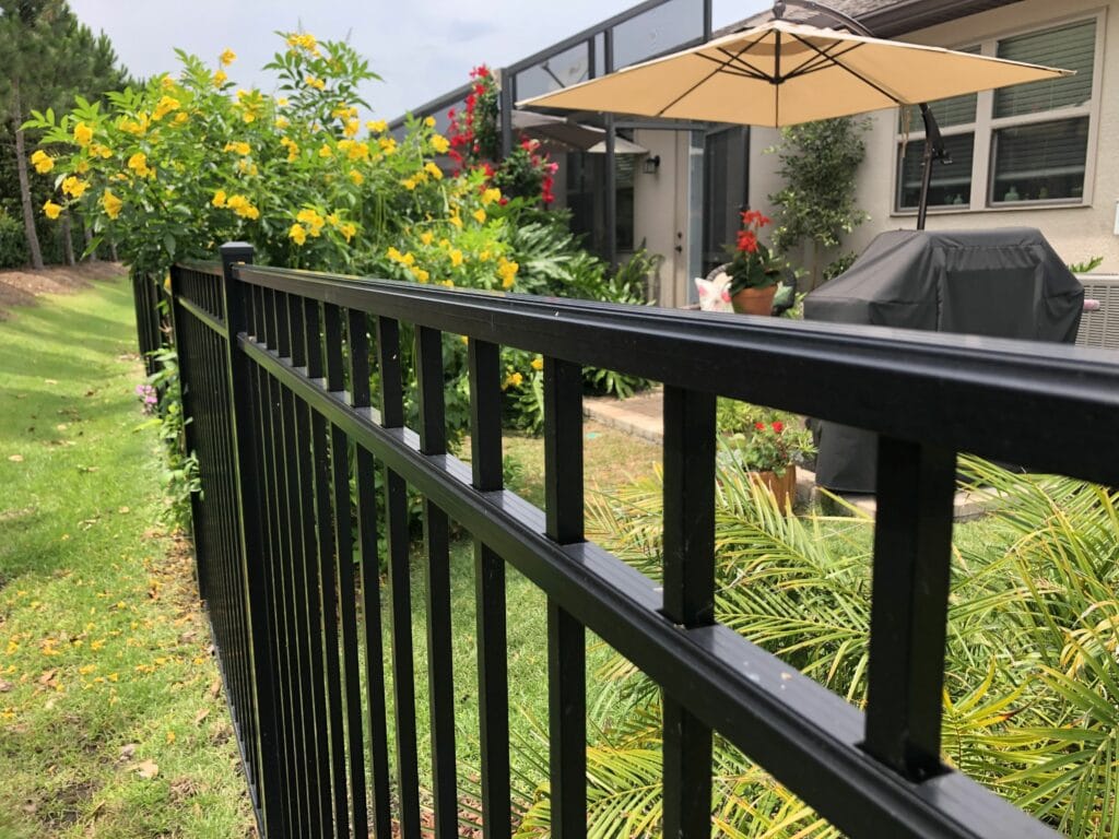 Backyard patio with bbq, umbrella and aluminum fence with climbing flowers.