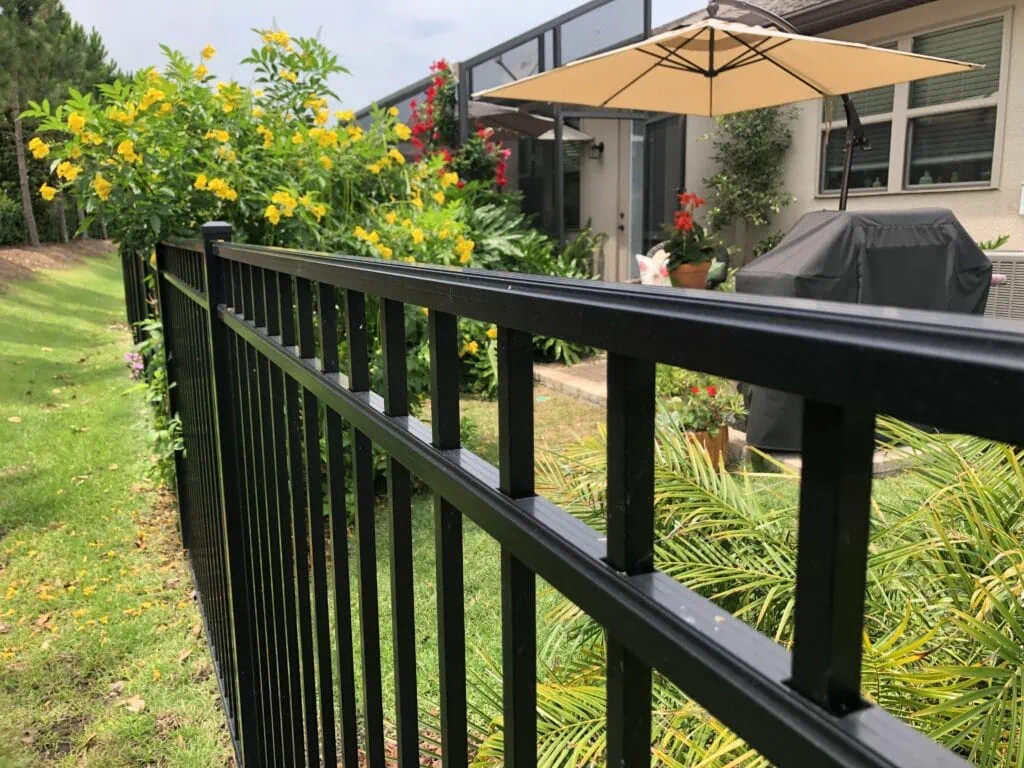 Backyard patio with bbq, umbrella and aluminum fence with climbing flowers.