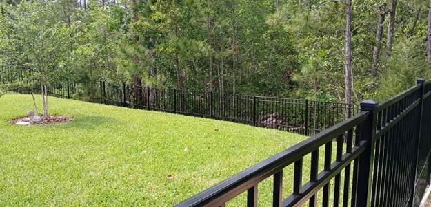 Large backyard with tree filled area and long puppy picket fence.
